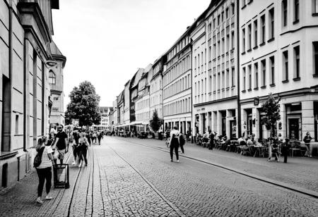 monochrome, instagram photo, a street in leipzig where i can see the westwerk on the right side. it's a summery atmosphere, in the afternoon at 16:00 and there are many people walking around on the street.