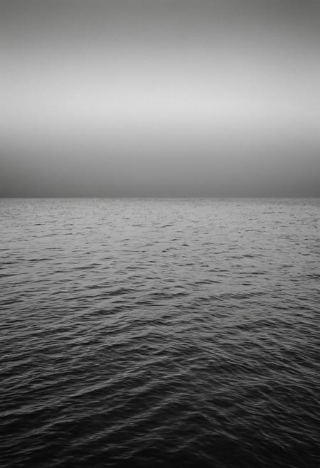 Experience the subtle power of "Whispering Waves," a minimalistic black and white seascape by Hiroshi Sugimoto. This photograph features a calm ocean, with gentle waves lapping at the shore under a vast, open sky. The horizon line is a simple, clean divide between the dark, textured water and the smooth, gradient sky. The minimalist approach, with its focus on the elemental forms and tonal contrasts, captures the quiet beauty and infinite expanse of the sea.