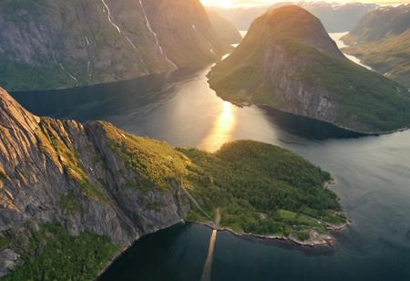 A from_above bird's-eye_view flying through a majestic fjord in Norway, summer, sunset