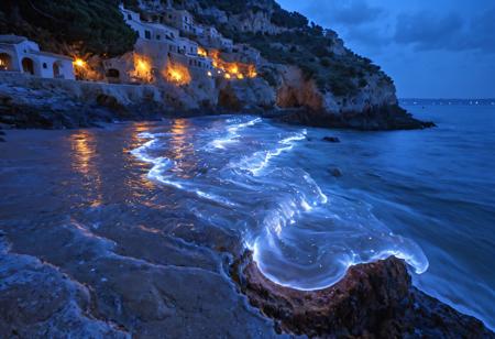 Bioluminescent waves crash against cliffs by a mediterranean seaside village. Bioluminescence, luminous
