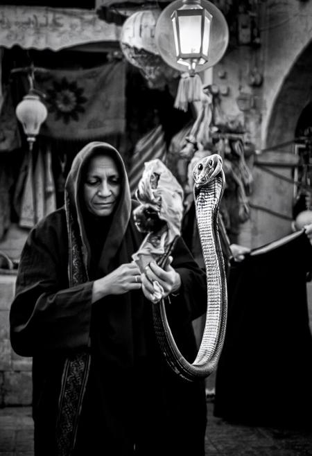 A  (((black and white photograph:1.8 ))) capturing a mystical scene of a Moroccan snake charmer in the souks, with a large snake weaving through the air, high light, high contrast, black and white, best quality, ultra highly details, 4k