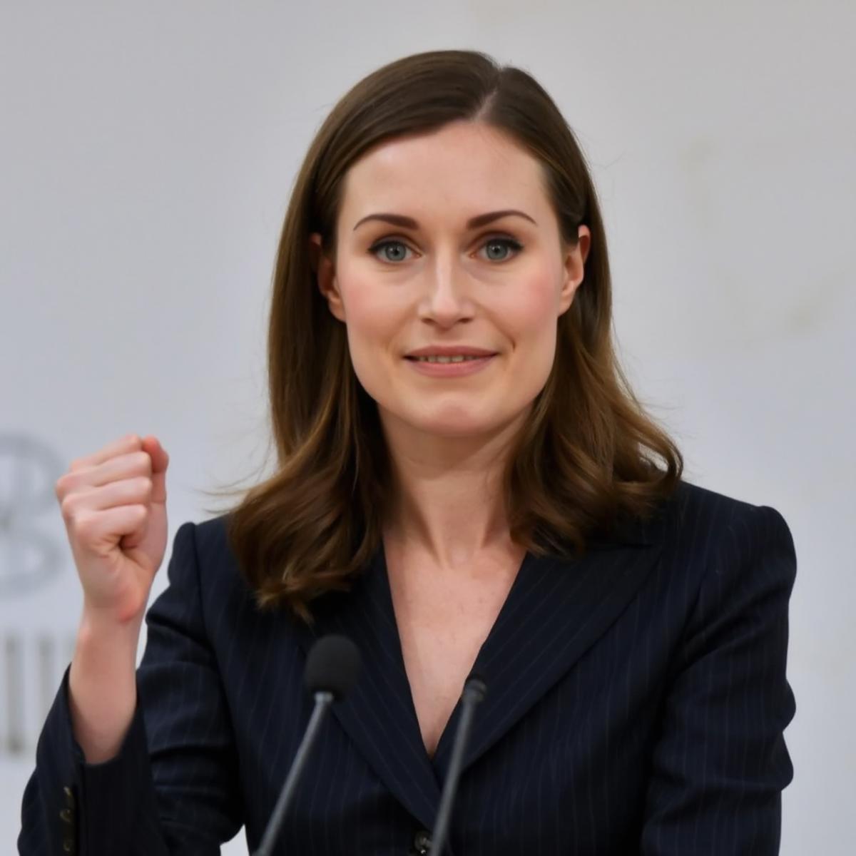 A photo of Sanna Marin wearing a formal outfit. She is giving a press conference, with a microphone in front of her, and waving her fist enthusiastically in the air