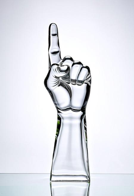 A clear glass sculpture of a raised fist showing the middle finger