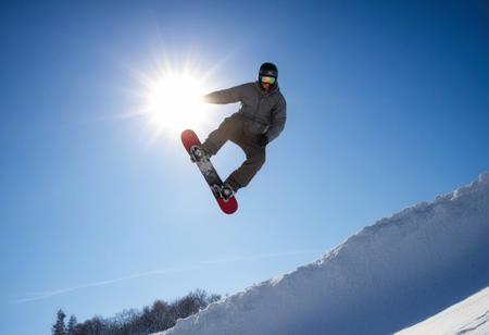 man doing a snowboard stunt, background a sunny blue sky
