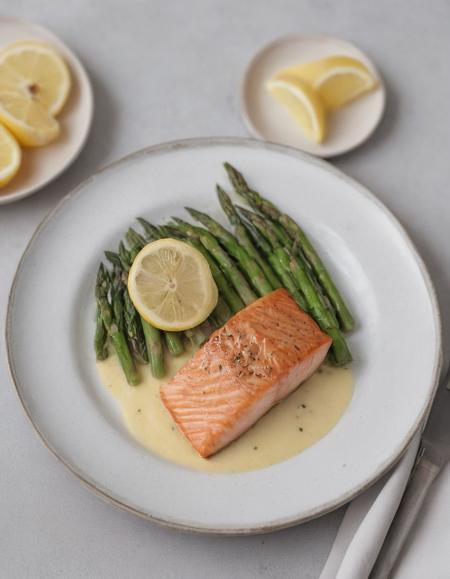 A beautifully plated gourmet meal with seared salmon, asparagus, and a lemon butter sauce, served on a white ceramic plate with garnish.