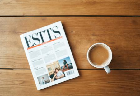 A view from the top of a wooden table with a coffee mug and a catalog, classic stock photo, chill vibe, latte cafe on a classic wooden kitchen table. Coffee mug on the far right. Clean mug with fresh coffee, light foam on coffee. No space between plank, glued plank without gaps. Oak coloured wood. Coffee mug should take 1/16 of the image. View from far above. Large table, small mug. Mug on top right corner. Tiny mug. Focus on table, not on mug. Mug should be on the right edge. Magazine centered on the image. Catalog on center and mug on top-right corner