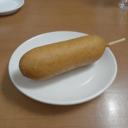 A photorealistic image of a delicious 9hotdog placed on a plate in a restaurant setting. The 9hotdog should be golden brown, with a crispy exterior and a juicy interior visible at one end where it's bitten off. The plate can be white or a light color to contrast with the golden hue of the 9hotdog. There might be a small dish of mustard or ketchup on the side for dipping. The table should have a clean tablecloth, and the lighting should be warm, highlighting the appetizing look of the 9hotdog. The background can have subtle hints of a restaurant ambiance, like a glass of water or some cutlery, <lora:cornhotdog:0.65>, (bottle of soda),<lora:applesoda:0.75>