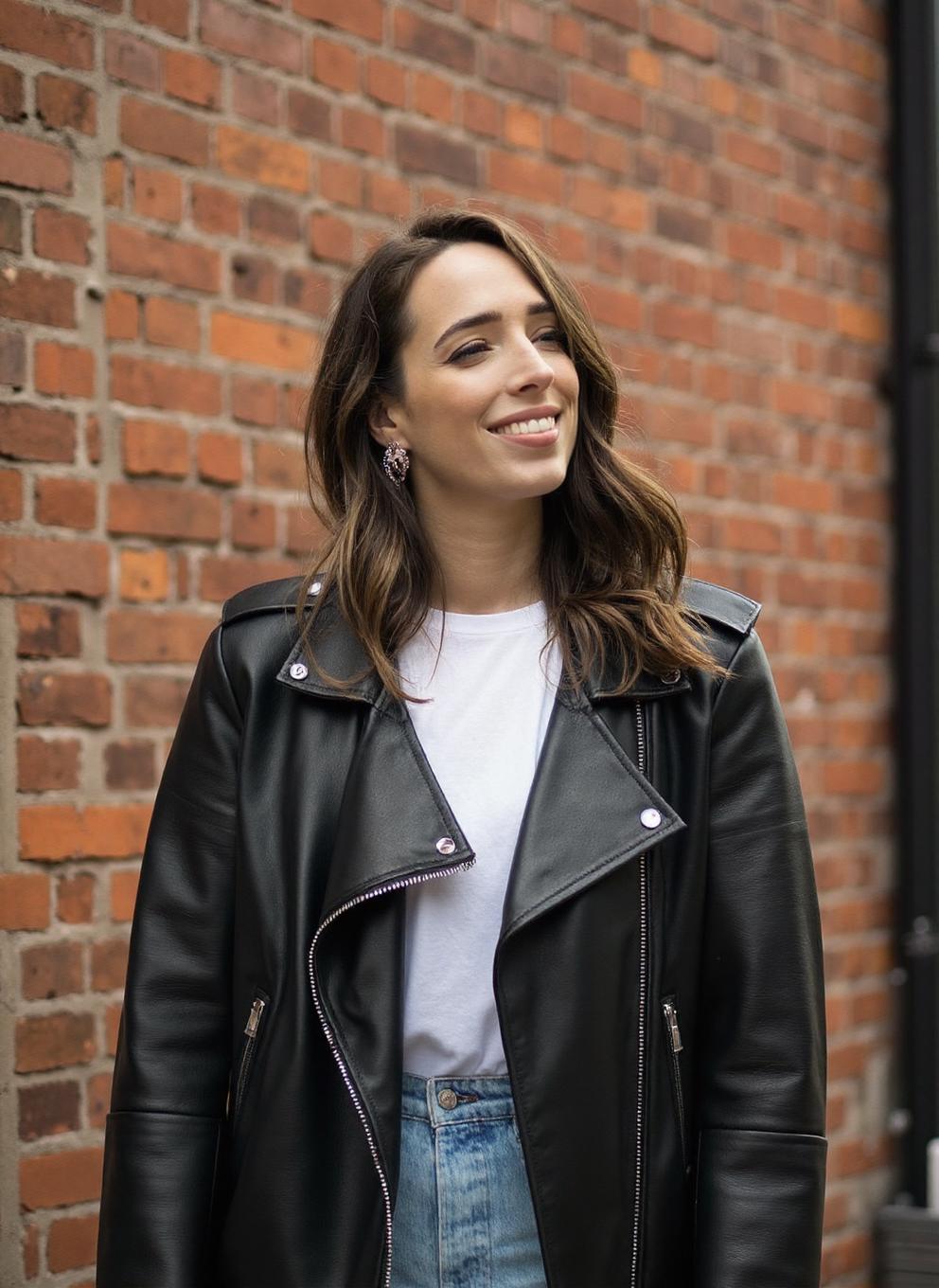 An exciting professional photograph of a 20yo young woman CiOD, wearing a leather jacket and white tshirt, standing in front of a brick wall, smile, pale skin, striking makeup, lipstick, detailed skin, bokeh, natural lighting, female focus, SFW, Instagram<lora:Ciara_ODoherty-000018:1>