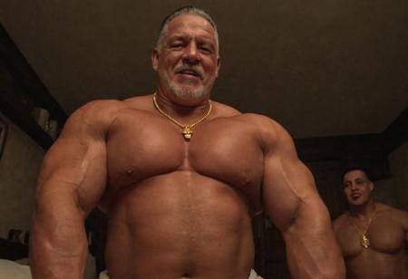 (photo, realistic, raw), (nighttime, at night, dark, dark hard shadows, cinematic atmosphere, movie grain, hazey atmosphere), gay porn, gay sex scene, closeup from below, focus on face, (brute, strongman, priest, european monk, cleric, holy, angelic, wise, gentleman, etherial, spiritual, emperor, king, god), old burly buff gentleman, goatee, old manly mature man, combed back hair,  doublechin, old tanned grandpa, wrinkly neck, proud big chest, thick neck, armpits, tanned skin, tight golden spandex, gold jewellery, gold necklace, in a dark cloister bedroom at night, nighttime,looking directly at viewer with a loving caring smile, leaning forward close to viewer, very close, intimite situation, romantic atmosphere, intimate lustful romantic expression, sad expression, belly and pecs from below, sweaty oily oiled skin