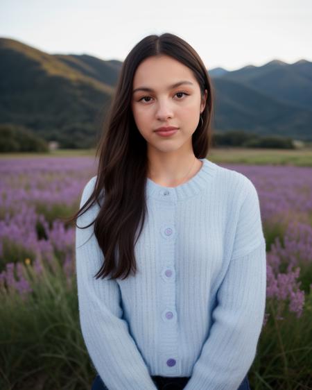 front on portrait of olivrod, looking at viewer, in field of purple flowers, hills, late afternoon, wearing light blue sweater <lora:olivrod:1>