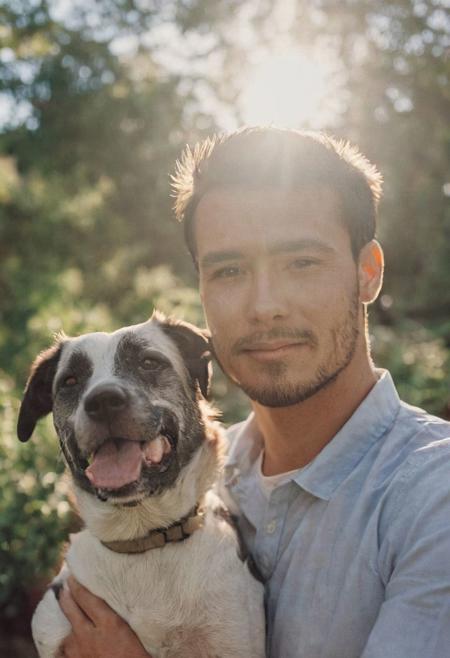 cinematic film still fashion photography portrait of 1man with cute dog as companion, headshot, sunlight , Fine Art & Beauty Photography – ,,light diffraction in frame, dreamy,hazy look.  Helios 44-2 lens mounted on a Praktica MTL 5B Helios 44M-4 lens, 58mm f/2,   in a garden. authentic happy smile towards camera, <lora:hand 4:0.3>