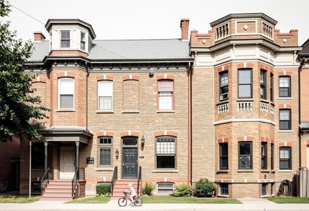 The five identical houses were built c. 1880 on land formerly part of a brickyard owned by George Wyatt, whose own house stands across the street. The facade of each house is divide vertically into two sections: the left one is flat, and is topped by a square turret roof, with a single story portico sheltering double entrance doors, and the right sight is a polygonal project bay rising the full three stories. The shallow roof cornices are studded with brackets. The bricks are multicolored with intricate design.  There is a small child riding her bike out front.