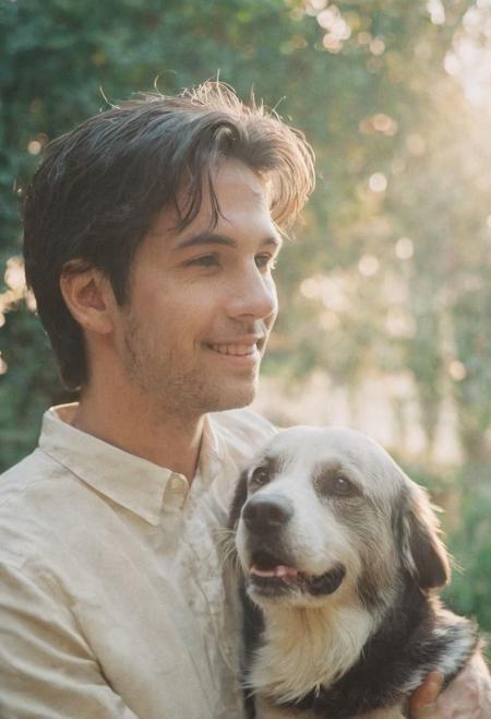 cinematic film still fashion photography portrait of 1man with cute dog as companion, headshot, sunlight , Fine Art & Beauty Photography – ,,light diffraction in frame, dreamy,hazy look.  Helios 44-2 lens mounted on a Praktica MTL 5B Helios 44M-4 lens, 58mm f/2,   in a garden. authentic happy smile towards camera, <lora:hand 4:0.3>