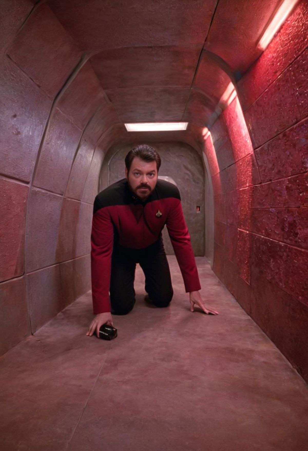 A man in a red shirt is crouching down in a small room.