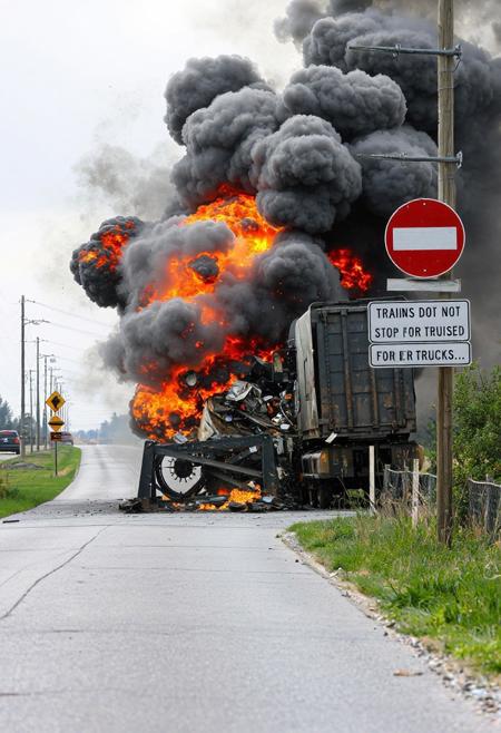 A road with a railway crossing, a freighttrain colliding with a big truck, breaking the truck in thousand pieces, the train and the truck go up in a big explosion. A sign reads : "Trains do not stop for trucks....".