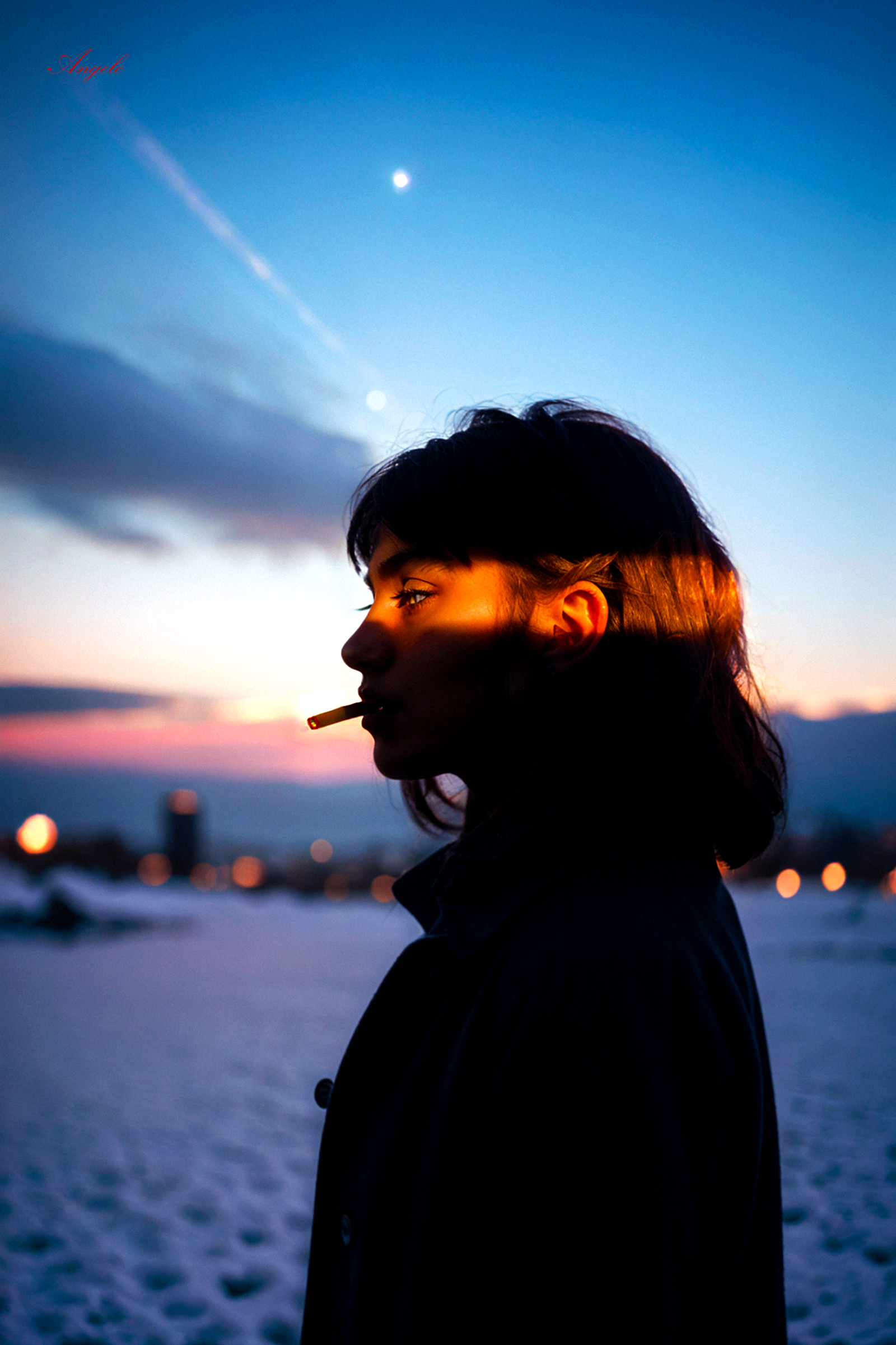 A woman smoking a cigarette while standing in the snow during a sunset.