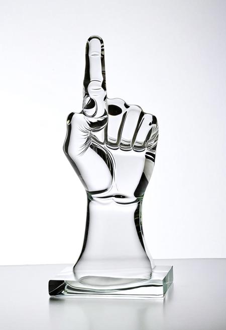 A clear glass sculpture of a raised fist showing the middle finger