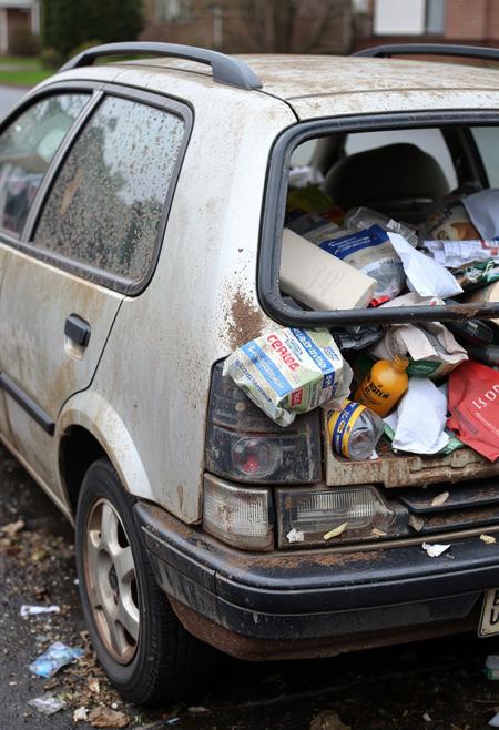A small car totally filled with common household trash, car is dirty and dented, trashed