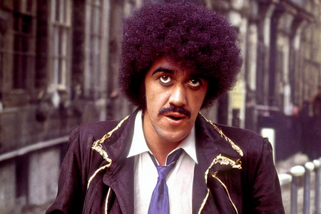 highres , color photograph, ThinLizzy, TLPhil is 1boy  with a big afro,  walking 1970s london streets,  detailed glossy eyes looking at viewer, visible skin pores,  dof<lora:TLPhil:1>