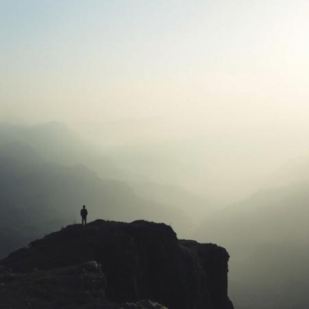 A vast, misty landscape at dawn, with mountains fading into the distance, symbolizing the expansive, emotive quality of post-rock music, with soft, ethereal lighting and a lone figure standing on a cliff, contemplating the view, dreamlike atmosphere, muted colors.