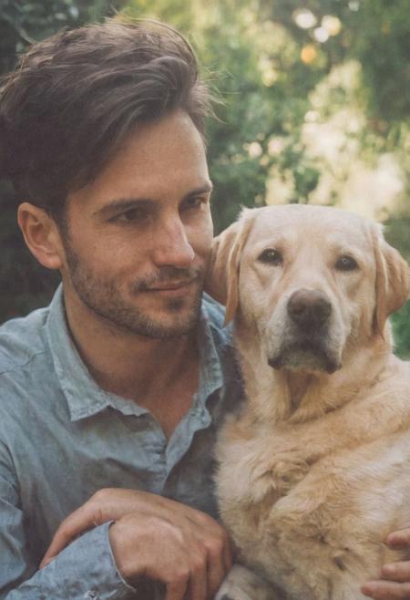cinematic film still fashion photography portrait of 1man with dog as companion, grainy, headshot, sunlight , Fine Art & Beauty Photography – ,,light diffraction in frame, dreamy,hazy look.  Helios 44-2 lens mounted on a Praktica MTL 5B Helios 44M-4 lens, 58mm f/2,   in a garden. authentic happy smile