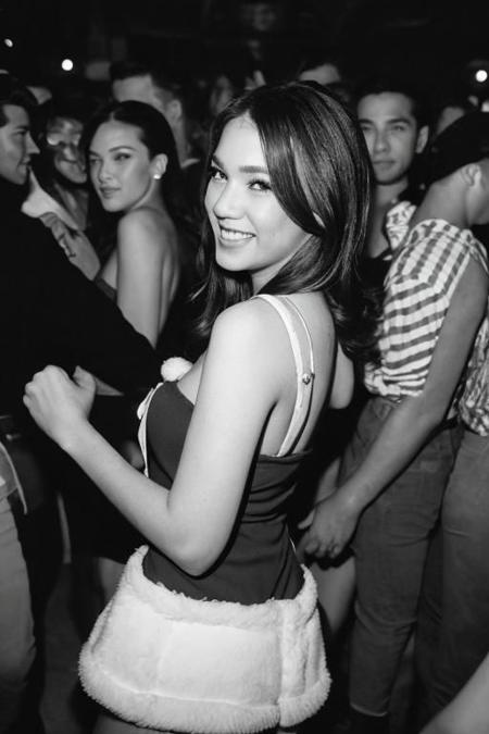 winter postcard, postcard style, white border,  of a close-up portrait featuring a girl in a santa dress, amidst a bustling dance floor in New York City's vibrant nightlife. Emphasize the sharpness of her face as the crowd dancing around her from behind while she laugh. Use a Nikon F4 camera and analog Ilford film for a vintage touch