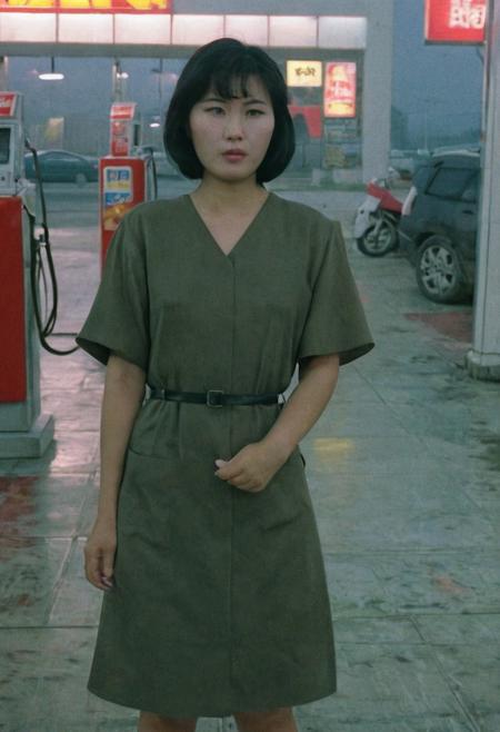 A North Korean female, with short black hair, wearing a v-neck army color dress, in a gas station, dusk, cloudy, foggy, North Korea, detailed, UHD, DSLR, the 1990s, VHS footage