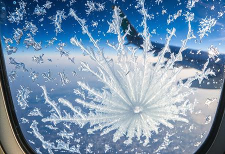 JNANX,luminous white silhouette,cyan glow,emerald highlights,flickering outline,dreamlike movement,
"A close-up view from an airplane window reveals intricate ice crystals forming on the outer pane. The blue sky and a portion of the aircraft's wing are visible in the background, distorted slightly by the frosty accumulation. Numerous delicate, feathery ice patterns spread across the window, with a denser, more concentrated cluster at the bottom center, almost appearing to grow upwards. Sunlight reflects off the icy surface, creating subtle glints. The overall impression is one of cold beauty, showcasing the unique atmospheric conditions encountered at high altitudes. The textures of the ice are varied, from fine dust-like particles to more defined, branching structures, suggesting a dynamic freezing process. The window itself has some minor smudges or imperfections, adding to the authenticity of the aerial perspective."