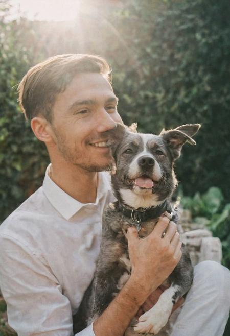cinematic film still fashion photography portrait of 1man with cute dog as companion, headshot, sunlight , Fine Art & Beauty Photography – ,,light diffraction in frame, dreamy,hazy look.  Helios 44-2 lens mounted on a Praktica MTL 5B Helios 44M-4 lens, 58mm f/2,   in a garden. authentic happy smile towards camera, <lora:hand 4:0.3>