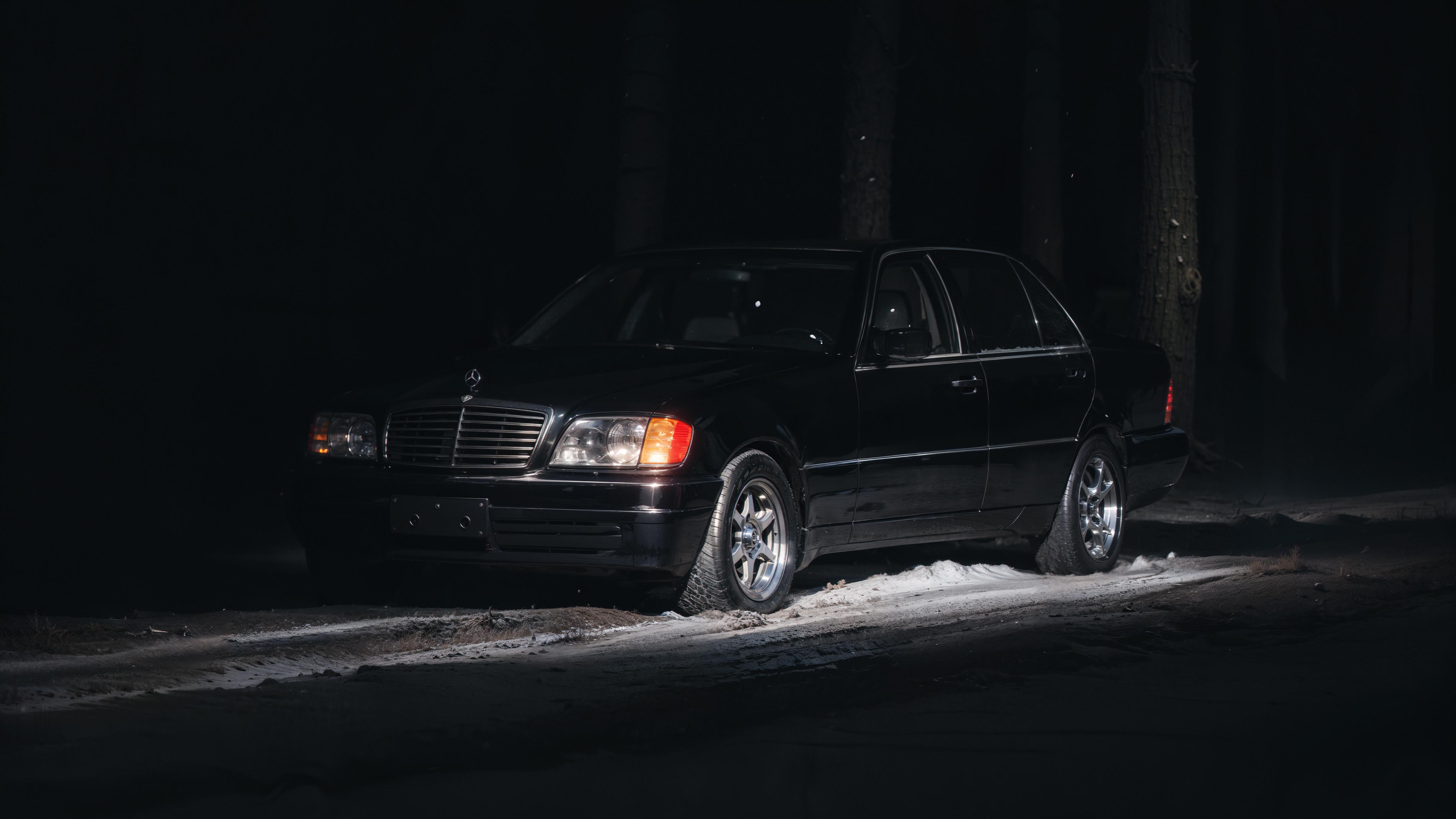 A black car on a dark road with snow on the ground.