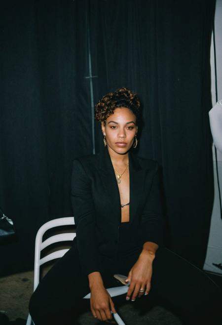 (gritty analog photo:1.2), candid (snapshot:1.2) of a sophisticated and cool 22-year-old biracial female hip-hop artist from Brooklyn sitting in a backstage room getting ready for her show, natural skin texture, realistic skin texture, (skin pores:0.8), (skin oils:0.8), (behind the scenes photography:1.2), documentary style photography, high contrast, deep shadows, hires, highly detailed, (film grain:1.2), the picture conveys effortless coolness, polaroid film photography