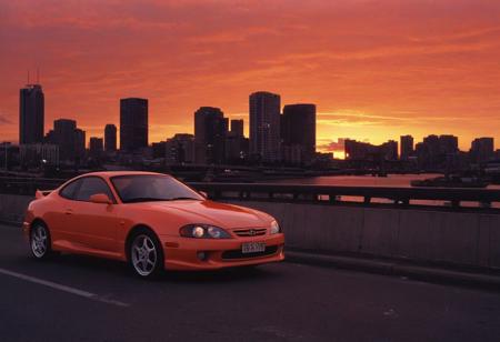 (1996 Hyundai Tiburon RD) motor vehicle, no humans, city, sky, outdoors, scenery, orange sky, road, building, cityscape, sunset, vehicle focus, skyscraper, sports car, shadow, gradient sky, red sky, evening, cloud, street, skyline, twilight, spoiler \(automobile\), orange background, dusk, red background, water, solo, bridge,