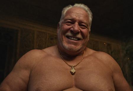 (photo, realistic, raw), (nighttime, at night, dark, dark hard shadows, cinematic atmosphere, movie grain, hazey atmosphere), gay porn, gay sex scene, closeup from below, focus on face, (brute, strongman, priest, european monk, cleric, holy, angelic, wise, gentleman, etherial, spiritual, emperor, king, god), old burly buff gentleman, old manly mature man, combed back hair,  doublechin, old tanned grandpa, wrinkly neck, proud big chest, thick neck, armpits, tanned skin, tight golden spandex, gold jewellery, gold necklace, in a dark cloister bedroom at night, nighttime,looking directly at viewer with a loving caring smile, leaning forward close to viewer, very close, intimite situation, romantic atmosphere, intimate lustful romantic expression, sad expression, belly and pecs from below