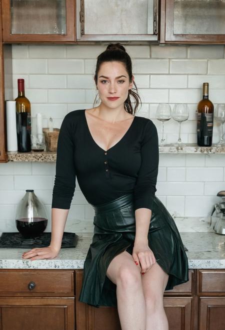 Film photograph taken in a nice suburban kitchen. Liv sits at the counter with a carafe of red line  and a stemless wine glass.
LIV wears a black skirt and white blouse, partially unbuttoned. Kitchen is all white tile and white wood. 
LIV is an  older attractive 45 year old woman. long brown hair parted sharply in the center, up in a messy ponytail, flowing down past shoulders. Italian heritage, resembling TYLER, LIV. smooth pale skin with makeup. thin trimmed Penciled eyebrows. thin lips, slight underbite and big chin and chubby cheeks, high cheekbones, rectangular shaped face, thicker neck, wide jaw. Dark cateye eyeliner and a few light freckles. 5 foot 3 inches tall and 200 pounds, thicker neck, full breasts with cleavage, high cheekbones, wide round nose. dark brownish Green eyes, bright smile showing gums. Thigh gap. Soft tummy