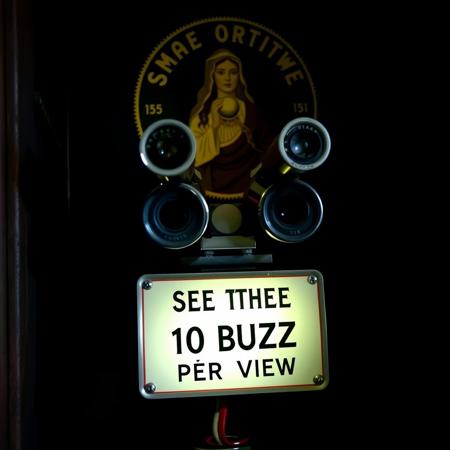 A coin operated stereo telescope binocilars in closed dark room with sign decorated with image of a female oracle holding crystal ball and text "SEE THE FUTURE" and "10 BUZZ PER VIEW"