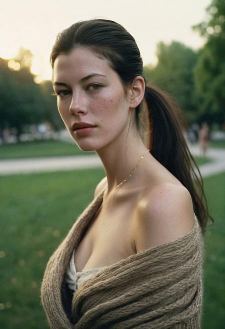 Grainy lowfi desaturated film photograph taken in a city park at dusk. Heavy Bokeh effect with focus on her green eyes, blurry background. A pretty young woman of northern Italian heritage wraps her brown cardigan around her bare shoulders. Goosebumps on a bare exposed shoulder. She wears the cardigan over a little summer sun dress and is chilly as the cool wind blows loose stands off her long black hair in her eyes. Tight ponytail. Fine Delicate thin gold chain necklace. She resembles Liv Tyler. The setting sun casts soft light into her eyes. Full soft cheeks and softer jawline, round chin, soft rounder oval face with the lightest freckles.