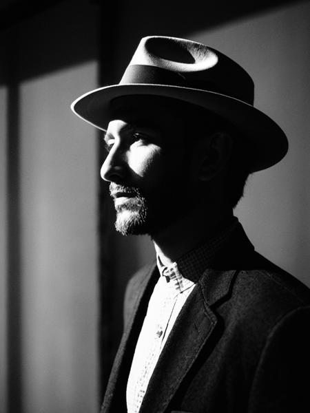 Portrait of a man with a fedora, in the style of chiaroscuro lighting, Sony α7, confident expressions, monochrome image, fine detail, Film Noir Influence, contemporary art, 35mm