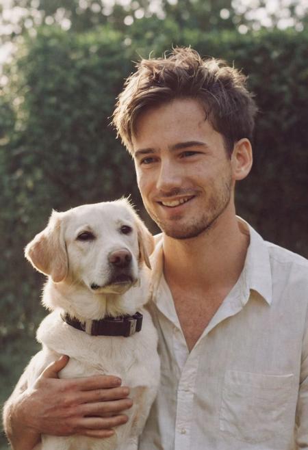cinematic film still fashion photography portrait of 1man with dog as companion, grainy, headshot, sunlight , Fine Art & Beauty Photography – ,,light diffraction in frame, dreamy,hazy look.  Helios 44-2 lens mounted on a Praktica MTL 5B Helios 44M-4 lens, 58mm f/2,   in a garden. authentic happy smile