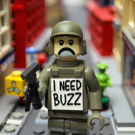 Plastic soldier make of clay holding sigh written ‘I NEED BUZZ’ in a miniature city like it's make of lego.