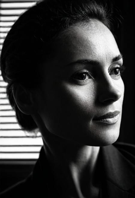 Close-up portrait of a woman, side-lit with dramatic shadow play, high-contrast black and white, soft-focus edges, Canon RF 85mm f/1.2L, ISO 100, f/2, 1/200 sec, natural light through blinds, moody, introspective expression, fine details, high-definition, shadow texture on skin. fluff on skin