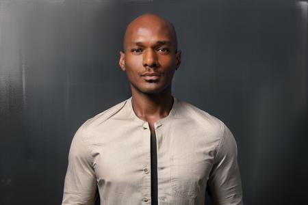 <lora:rhyheimsv3:1> rhyheims, black man, bald, dark skin, brown eyes, professional studio quality modeling headshot, 4K, simple dark background, dramatic lighting, neutral expression, realistic skin, fine detail, shirt, ultra realistic photograph, professional photograph, by Gucci photographer.