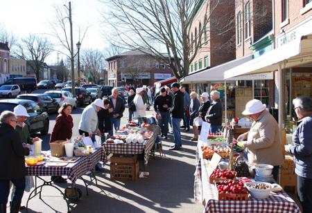 small town Saturday market day, sunny, northerly, crisp, tables, booths, crafts, homemade food, carvings, buyers, sellers, colorful, chocolate sop, bakery, parked cars, produce, berries, pottery, wool weaving, hot dog grilling, bookstore, bank building, tea room