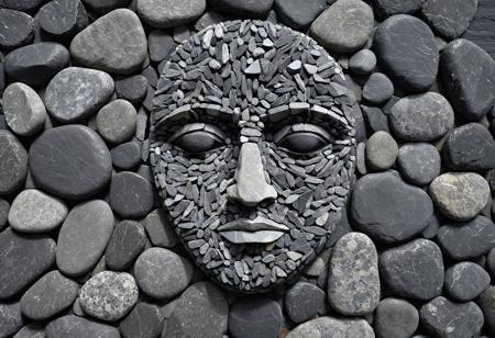 Top down photograph of a (human face) created from stones in black and grey colors, meticulously arranged on a slate rock background