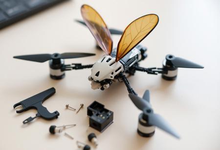 photographic image of disassembled micro-drone robotic bug, with wings. small, intricate parts scattered upon table,