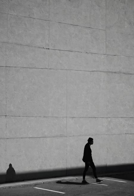 Capture the shadow of a person against a plain wall, focusing on the shape and movement. Use a Sony A7 III with a Sony FE 50mm f/1.8 lens at f/2.0, 1/125s, ISO 100.