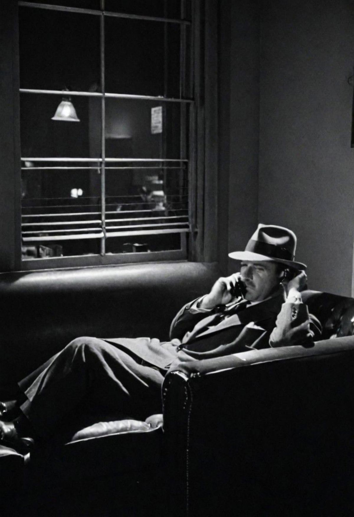 Man in a suit and hat sitting on a couch talking on his cell phone.