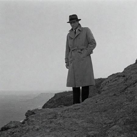 1950s detective film, mysterious man in a trenchcoat standing at the edge of a cliff after murdering a man whos corpse lies next to him. Captured on a 35mm camera, black and white, classic film noir film.