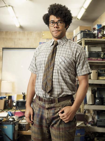 Richard Ayoade as Moss, parted afro, plaid_shirt, paisley tie, tweed_pants, photo middle-aged man in cluttered office, basement office, (masterpiece:1.2) (photorealistic:1.2) (bokeh) (best quality) (detailed skin) (intricate) (8k) (HDR) (cinematic lighting) (sharp focus) <lora:Richard-Ayoade-v10:0.7>