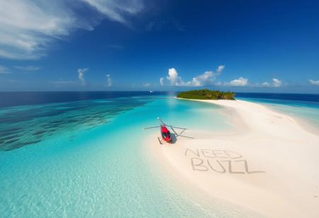 Helicopter aerial view of tropical desert island beach where there is written text on sand by a survivor "NEED BUZZ"