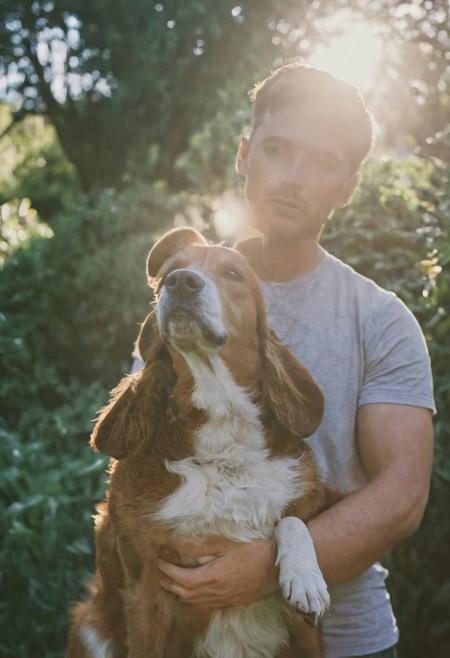 cinematic film still fashion photography portrait of 1man with dog as companion, grainy, headshot, sunlight , Fine Art & Beauty Photography – ,,light diffraction in frame, dreamy,hazy look.  Helios 44-2 lens mounted on a Praktica MTL 5B Helios 44M-4 lens, 58mm f/2,   in a garden.